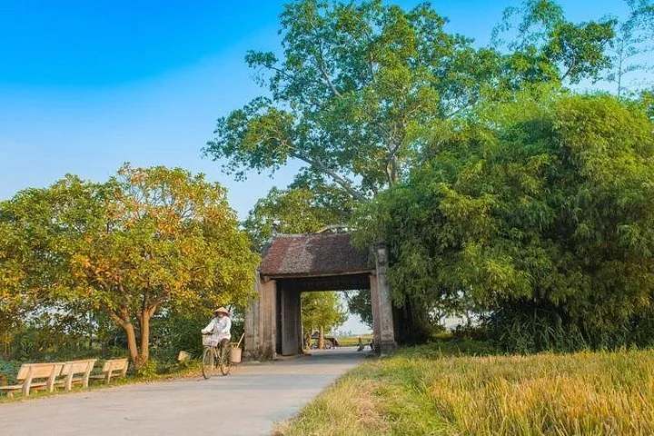 Una persona in bicicletta attraversa una vecchia porta del villaggio circondata da alberi.